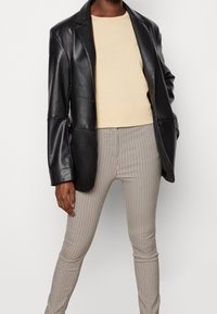 Sort læderblazer med en struktureret design, parret med en lys beige tætsiddende top og skinny bukser med ternet mønster i brun og hvid.