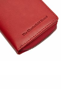 Portafoglio in pelle rossa con superficie strutturata, logo in rilievo e zip di colore argento lungo il bordo. Forma compatta e rettangolare.