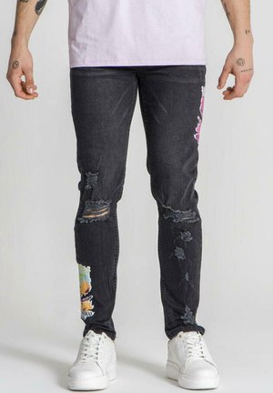 Jeans de mezclilla oscura con detalles desgastados, que presentan parches coloridos y rotos. Combinados con zapatillas blancas para crear contraste.