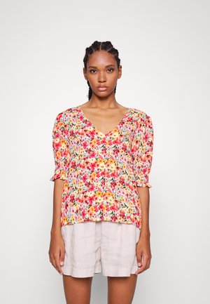 Blusa floral com decote em V, mangas bufantes curtas e um padrão de flores multicoloridas sobre um fundo claro; combinada com calções beiges.