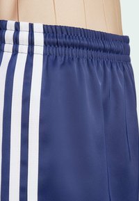 Mornarske sportske kratke hlače izrađene od sjajne tkanine s elastičnom pojasom. Imaju tri bijele pruge duž strana i suptilne nabore.