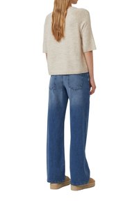 Suéter beige de punto con mangas cortas combinado con jeans de pierna ancha de color azul claro. El conjunto presenta un ajuste relajado y un diseño sencillo.