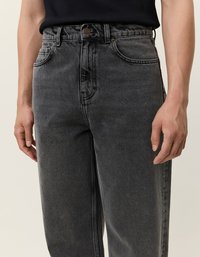 Čierne džíny z denimu so strihom rovného nohu, dizajnom s piatimi vreckami a jemným vyblednutím. Obsahujú klasické gombíkové zapínanie v páse.