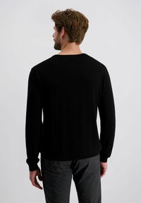 Zwarte lange-sleeve trui met ronde hals en geribbelde manchetten, met een zachte textuur. Draagt met donkergrijze broek, gezien vanuit de achterkant.