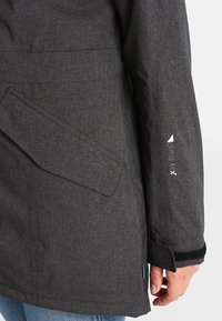 Veste noire résistante aux intempéries avec une finition texturée, dotée d'une poche latérale et d'un logo sur la manche. Conçue pour la fonctionnalité et le confort.