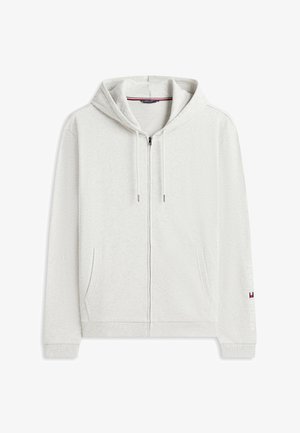 Sweat à capuche gris clair zippé avec cordons de serrage, poches frontales, poignets côtelés et logo discret sur la manche gauche près du poignet.