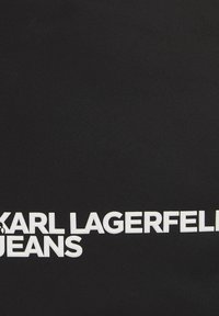 Musta kangas, jossa on rohkeaa, valkoista tekstiä, jossa lukee "KARL LAGERFELD JEANS." Kankaan pinta on sileä ja siinä on kevyt kiilto.
