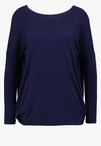 Tummansininen, pitkähihaista, väljä paita, jossa on leveä pyöreä kaula-aukko ja roikkuneet olkapäät tasaisella taustalla.