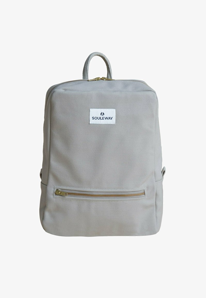 Grå canvasryggsäck med en dragkedjeförsedd framficka, gyllene dragkedjeaccenter och ett handtag på toppen. Har en vit logotypetikett på framsidan.