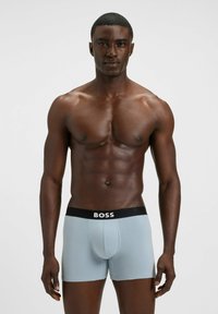 Boxer brief azzurri realizzati in tessuto liscio con una cintura nera con il logo "BOSS". Il design è aderente e arriva a metà coscia.