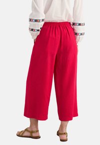 Crvene lanene culottes s elastičnom waistbandom, s širokim krojem i rubom koji pada do sredine teladi. Uparene su s smeškim sandalama.