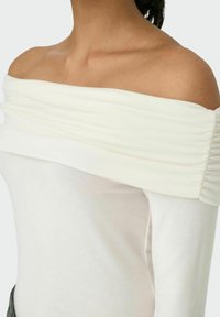 Off-the-shoulder top i hvid bomuldsblanding med rynket stof ved halsen, der har en tætsiddende silhuet og glat tekstur.
