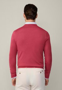 Roter Strickpullover mit langen Ärmeln, rundem Halsausschnitt und gerippten Bündchen. Hellblaues Kragen ist darunter sichtbar. Schlichtes Design, keine Muster.
