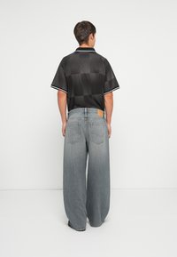 Czarna koszulka polo z krótkim rękawem w kratkę i białymi wykończeniami, zestawiona z oversize'owymi jasnoszarymi dżinsami z tylnymi kieszeniami.