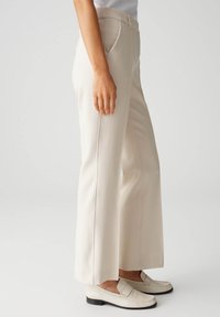 Beige wijde broek van gladde stof, met een hoge taille, zijzakken en nauwkeurige stiksels langs de naden.