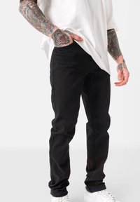 Czarne jeansy o slim fit, z pięcioma kieszeniami, lekkim streczem i subtelnymi detalami, w połączeniu z białymi trampkami.