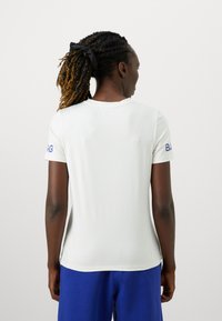 Valge sportlik T-särk lühikeste varrukatega, sobiva disainiga ja sinise logoga paremal varrukal. Sile tekstuur ja ümar kaelus.