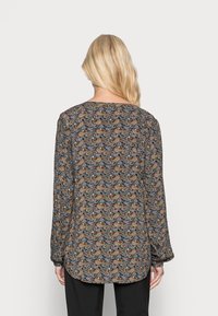 Musterbluse mit langen Ärmeln, abgerundetem Saum und einem aufwendigen Paisleymuster in Blau, Braun und Creme auf dunklem Hintergrund.