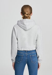 Felpa grigia accorciata con cappuccio regolabile, orlo a costine e maniche lunghe, abbinata a jeans blu con tasche posteriori e una vestibilità aderente.