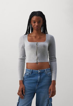 Hallitusroheline ribastuseta crop-top pikkade varrukatega ja ruudukujulise kaelusega, millel on ees lukk ringikujulise tõmblukuga. Kanda siniste teksapükste koos.