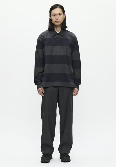 Langsleevige, collared shirt met donkergrijze en zwarte horizontale strepen, gecombineerd met losse donkergrijze broek en zwarte sneakers.
