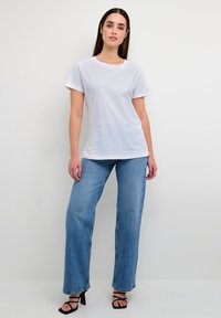 Hvid bomulds t-shirt med korte ærmer, parret med højtsiddende lyseblå jeans. Sorte strop-sandaler med høje hæle fuldender looket.