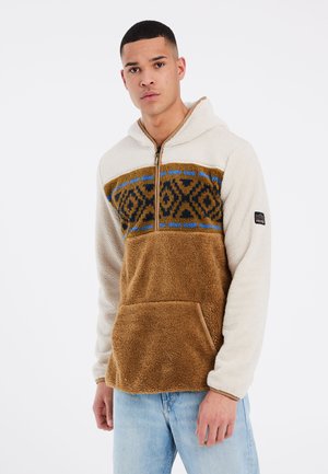 Hellbrauner und cremefarbener Hoodie mit Reißverschluss und Fronttasche. Verfügt über ein geometrisches Muster in Braun und Blau über der Brust. Weiche Textur.