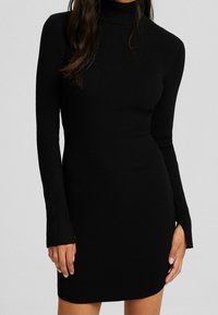 Robe longue à manches longues en tricot côtelé noir avec un col montant, une coupe ajustée et des fentes latérales aux manches, présentant une texture lisse.