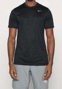 Černé sportovní tričko s krátkým rukávem a kulatým výstřihem, vyrobené z hladké látky, s malým šedým logem Nike na levé hrudi.