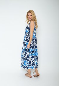 Niebieska i biała sukienka maxi w wzory, bez rękawów, z marszczoną talią. Posiada zwiewną spódnicę i lekką tkaninę.
