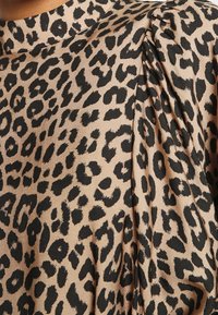 Látka s leopardím potiskem s černými skvrnami na béžovém pozadí, s plisovanou texturou a designem s vysokým límcem.