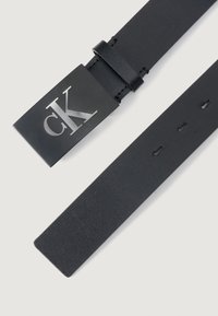 Curea din piele neagră cu o cataramă rectangulară și un logo metalic "CK". Textură netedă, ajustabilă cu mai multe găuri.