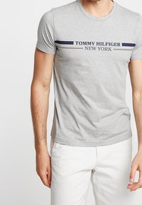 Grau Baumwoll-T-Shirt mit Rundhalsausschnitt, kurzen Ärmeln und einem blau-roten gestreiften Logo, auf dem "TOMMY HILFIGER NEW YORK" steht.