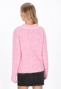 Rosa Strickpullover mit strukturierter Oberfläche und einem weißen, gewellten Kragen. Das Design zeichnet sich durch lange Ärmel und eine lockere Passform aus.