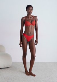 Rode bikini set met een gevormde beha en bijpassende lage slip. Gladde textuur, minimalistisch ontwerp en verstelbare bandjes.
