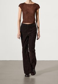 Ruskea lyhyt neulepaita yhdistettynä tummanruskeisiin kangashousuihin, joissa on leveät lahkeet. Asusteessa on tekstuuripinta ja tiukka siluetti.