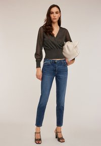 Szary top z dopasowanym talią i prążkowanymi długimi rękawami, zestawiony z medium-niebieskimi dżinsami i sandałami na obcasie z paskami.