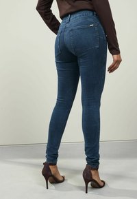 Mörkblå denim skinny jeans med hög midja, bakfickor och kontrasterande sömmar, i kombination med mörka klacksandaler.