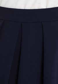 Jupe plissée bleu marine en tissu doux. Elle présente une taille lisse et des plis verticaux, conférant une apparence structurée.