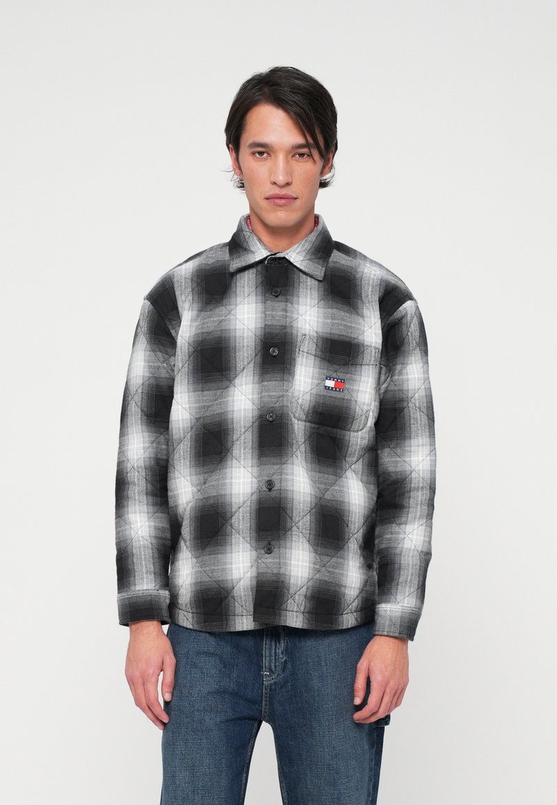 Kockás, steppelt flaneling fekete-fehér színben, gombos elejével és logópacsos mellzsebbel. Farmernadrág egészíti ki a megjelenést.