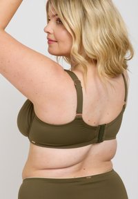 Olivgrön bh med slät tyg, justerbara band och en hake-och-ögon knäppning. Har subtila detaljer i guld.