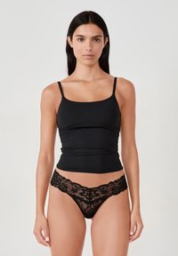 Camiseta sin mangas negra con tirantes delgados; tela suave y elástica. Combinada con un tanga negro de encaje con patrones florales y bordes ondulados.