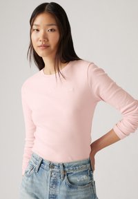 Lichtroze longsleeve shirt met een ronde hals en textuurstof, gecombineerd met hoge, versleten denim shorts. Eenvoudige logodetail.