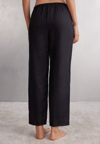 Zwarte linnen broek met een wijduitlopende snit en een elastische tailleband, met een gladde textuur en minimale details, gezien vanaf de achterkant.