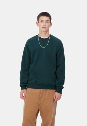 Dark green sweatshirt with ribbed cuffs and hem, featuring a crew neckline and raglan sleeves. Worn with light brown corduroy pants.