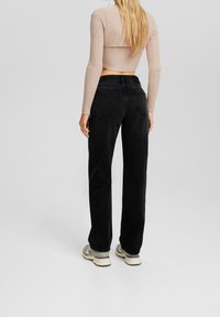 Jeans negros de tiro alto con corte recto y bolsillos traseros, combinados con un suéter corto de punto beige y zapatillas grises.