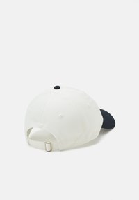 Bílá baseballová čepice s námořnickým kšiltem, nastavitelným popruhem vzadu a černým knoflíkem nahoře. Bavlněná tkanina. Jednoduchý design.