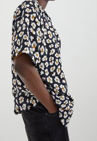 Black short-sleeve shirt with floral print in white, orange, and green. Soft fabric, loose fit, classic collar, and button detail.