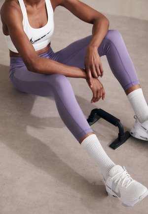 Sports bra in white with black logo, paired with light purple leggings featuring mesh panels. White ribbed socks and white athletic shoes.