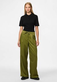 Zwarte poloshirt met korte mouwen, gecombineerd met groene wijde, gestreepte broek met een gestrikt tailleband en zwarte schoenen.